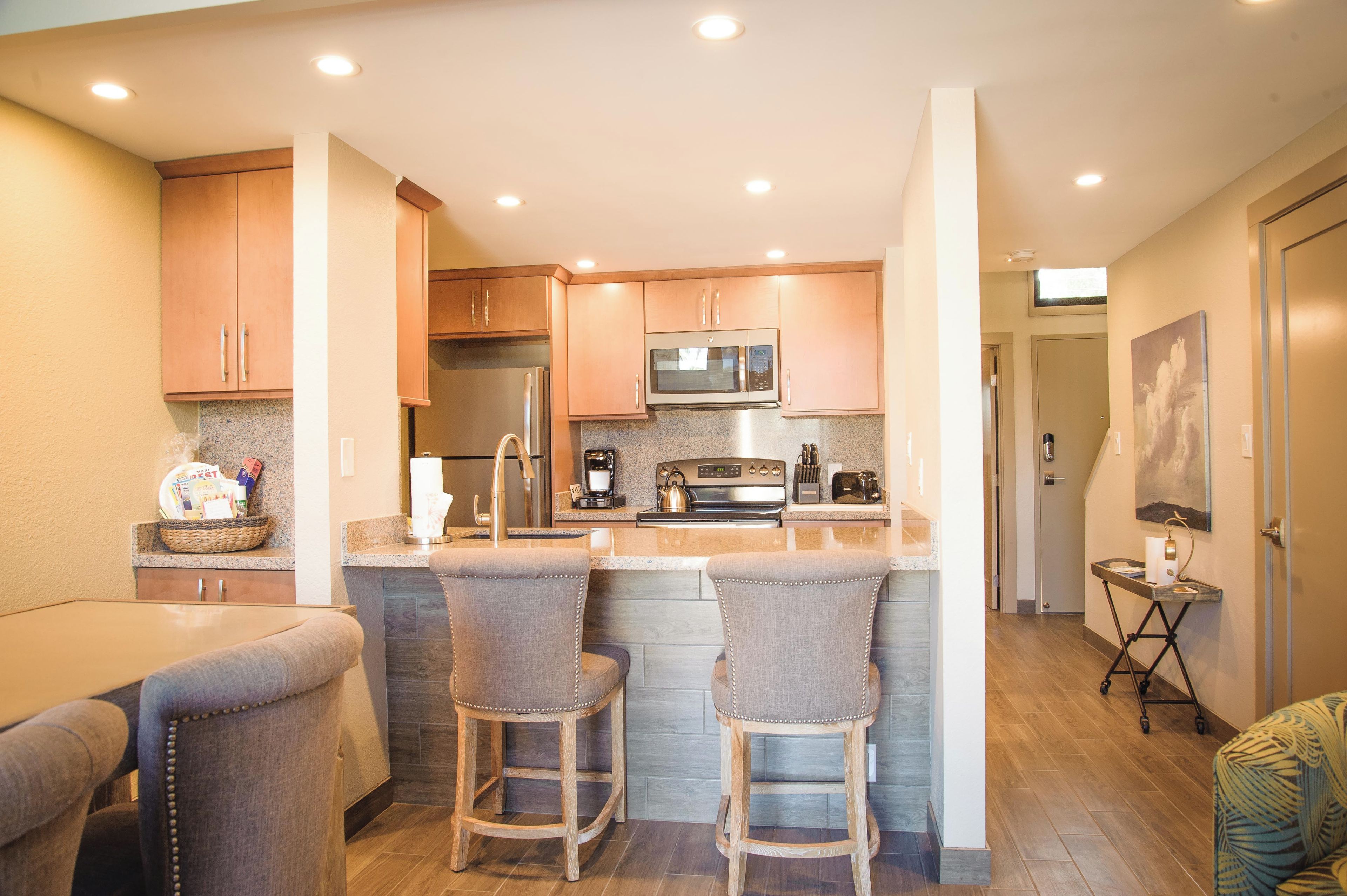 A compact kitchen with a central island, stainless steel appliances, and a dining area with two bar stools.