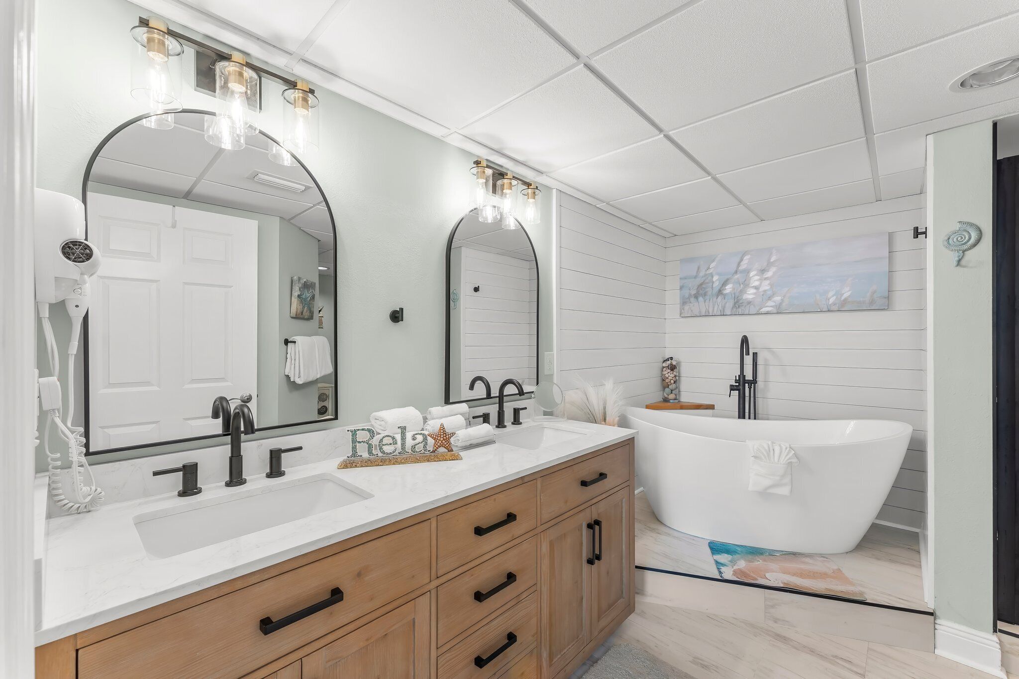 A modern bathroom with a freestanding bathtub, a double vanity with a large mirror, and a ceiling with recessed lighting.