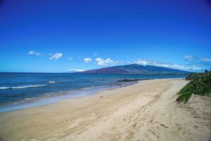 A beach with a mountain in the background, clear skies, and calm sea.