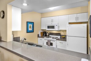 Una cocina compacta con armarios blancos, un microondas, una estufa y un refrigerador.