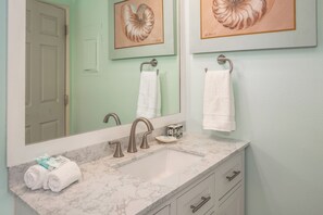 Un baño con lavamanos de mármol, dos grifos, un espejo y dos obras de arte enmarcadas.
