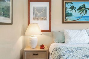 A neatly made bed with a patterned bedspread, a bedside lamp, and a framed picture of a beach scene.