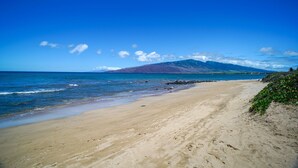 Une plage avec une montagne en arrière-plan, un ciel dégagé et une mer calme.