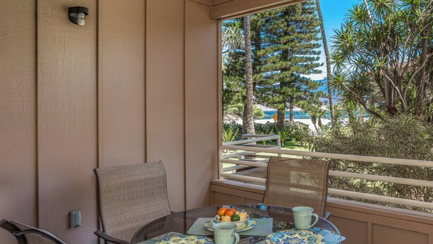Un balcon avec une table dressée pour deux personnes, agrémentée d’un saladier de fruits et d’une tasse.