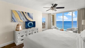 Habitación de hotel con una cama grande, ventilador de techo, televisión, cómoda y vista al océano.