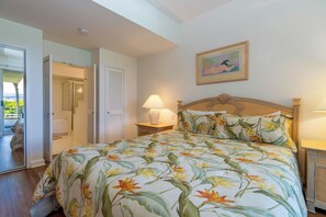 A bedroom with a bed, a nightstand, a lamp, a door, and a framed picture on the wall. - Vista Waikoloa Condo w/ Mountain Views - Walk to Beach! (Waikoloa)