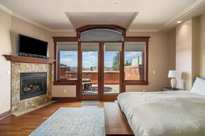 Un dormitorio con chimenea, televisor, ventana grande y cama.