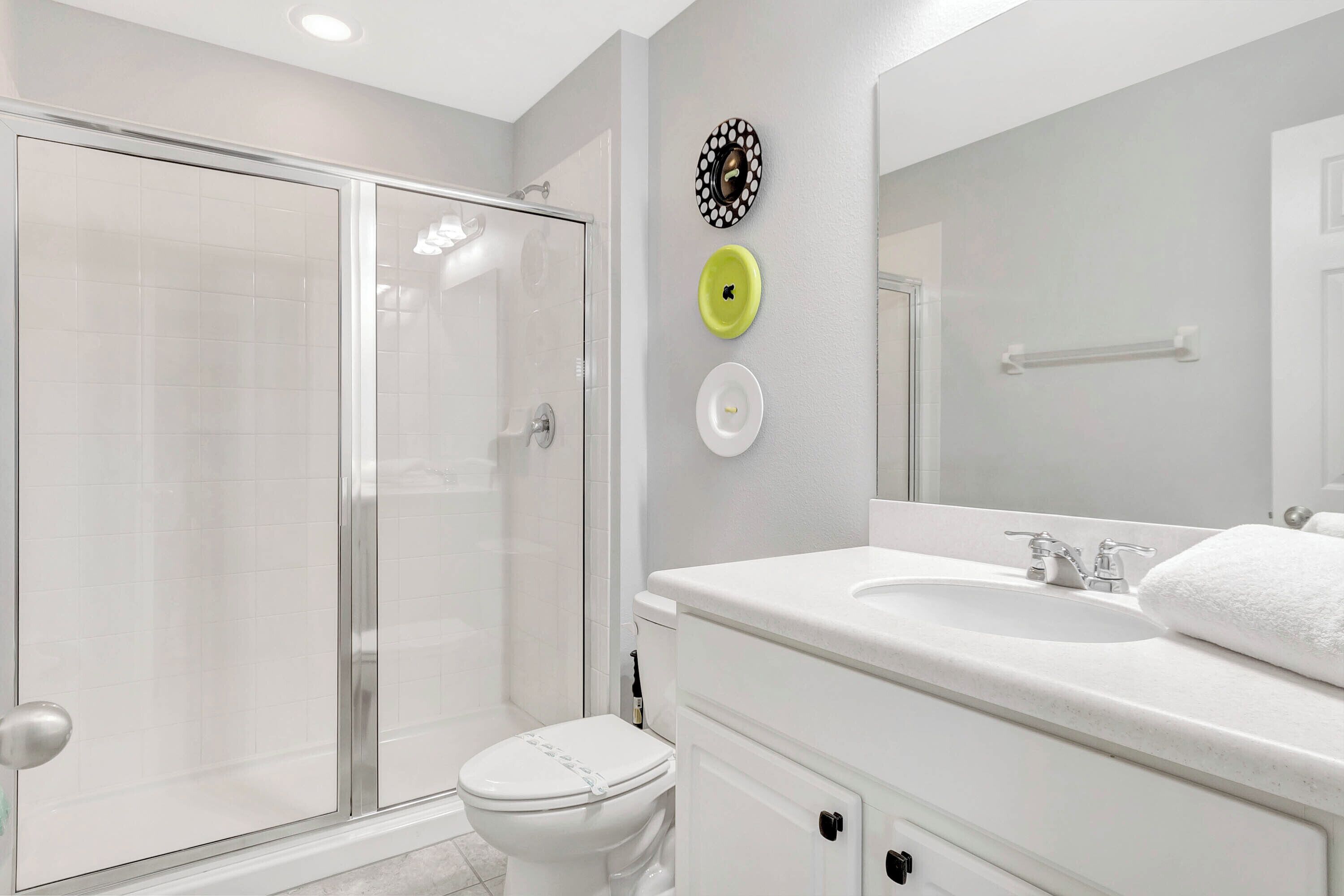 Une salle de bain moderne avec une douche à parois de verre, des toilettes blanches et un meuble-lavabo avec un miroir.