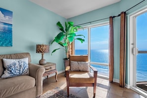 Ein Wohnzimmer mit Blick auf das Meer, ein Holzstuhl, eine Lampe und eine Pflanze.