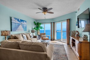 Ein geräumiges Wohnzimmer mit einer großen Couch, einem Deckenventilator und Meerblick durch große Glasüren.