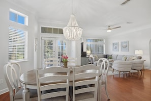 A spacious dining area with a chandelier, a dining table with chairs, and a view of the outdoors through large windows. - 3BR Beach Villa Near Pool! New 6-Seater GOLF CART, Screened Porch, Beach Tram (Miramar Beach)