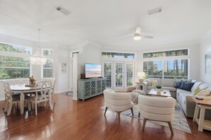 A spacious living room with a dining area, a television, and a ceiling fan. - 3BR Beach Villa Near Pool! New 6-Seater GOLF CART, Screened Porch, Beach Tram (Miramar Beach)