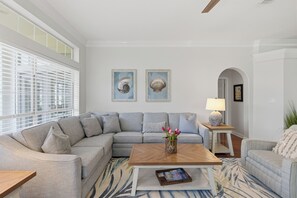 A living room with a sectional sofa, a coffee table, and two framed seashells on the wall.