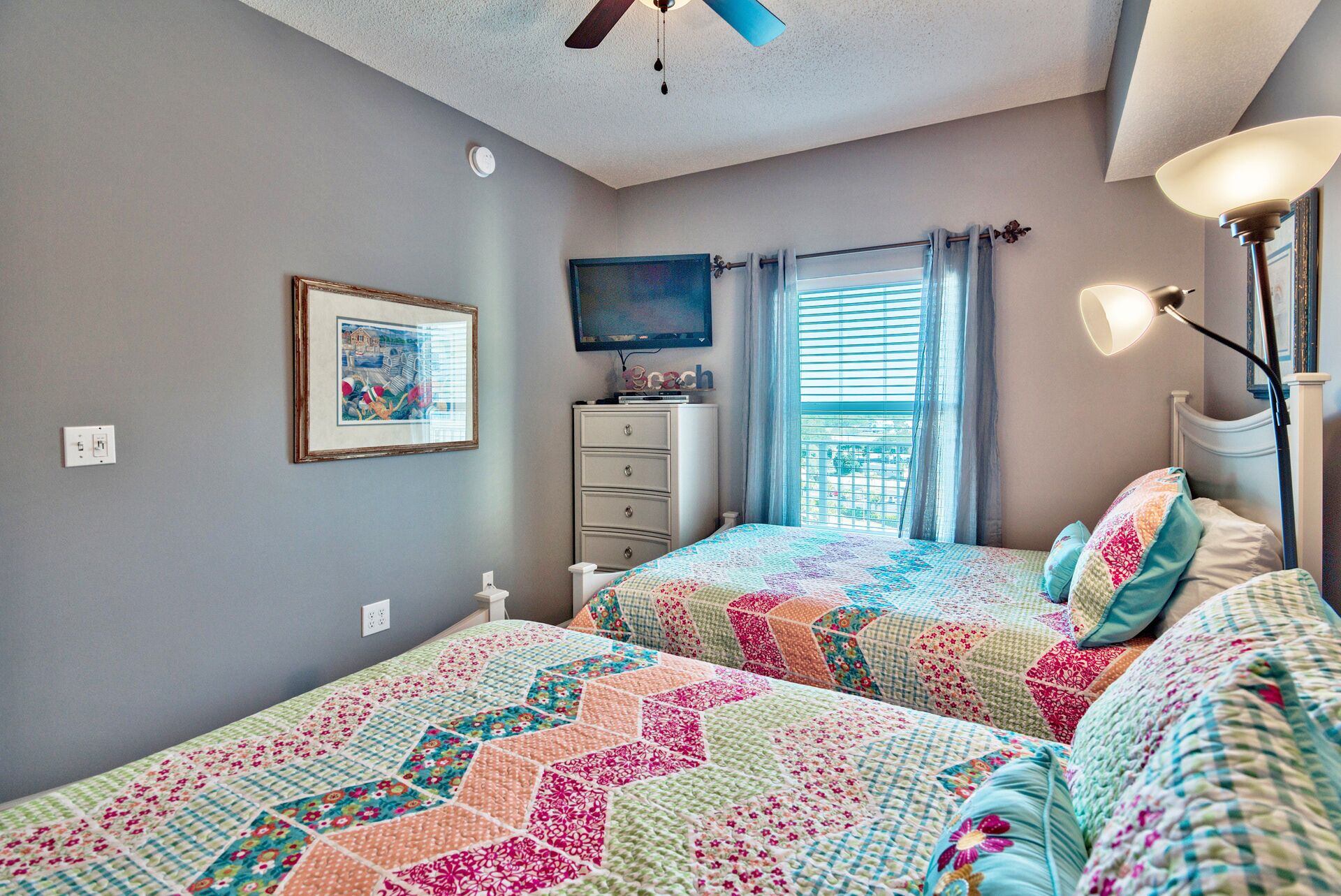 A bedroom with two beds, a dresser, a television, and a window with curtains.