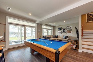 A pool table in a room with large windows, a sofa, and framed pictures on the wall.