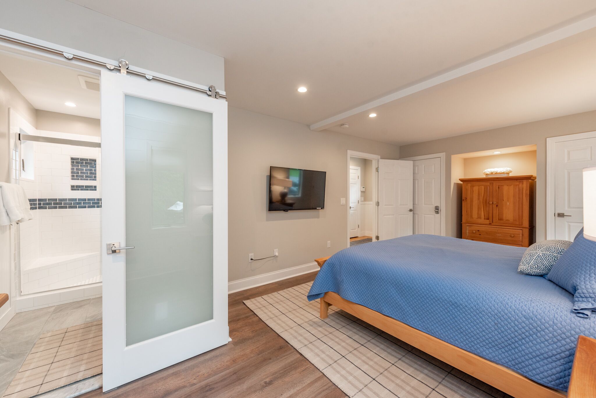 Een slaapkamer met een bed, een televisie, een houten kast en een badkamer met douche en bad.