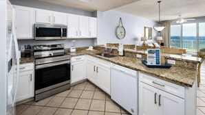 A modern kitchen with white cabinets, stainless steel appliances, granite countertops, and a view of the ocean.