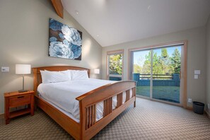 A bedroom with a wooden bed, a nightstand, a large window, and a view of the outdoors. - 3 Mulligan - Hot Tub with Wooded Views, Wine Cellar, SHARC passes, Comfort & Style (Sunriver)