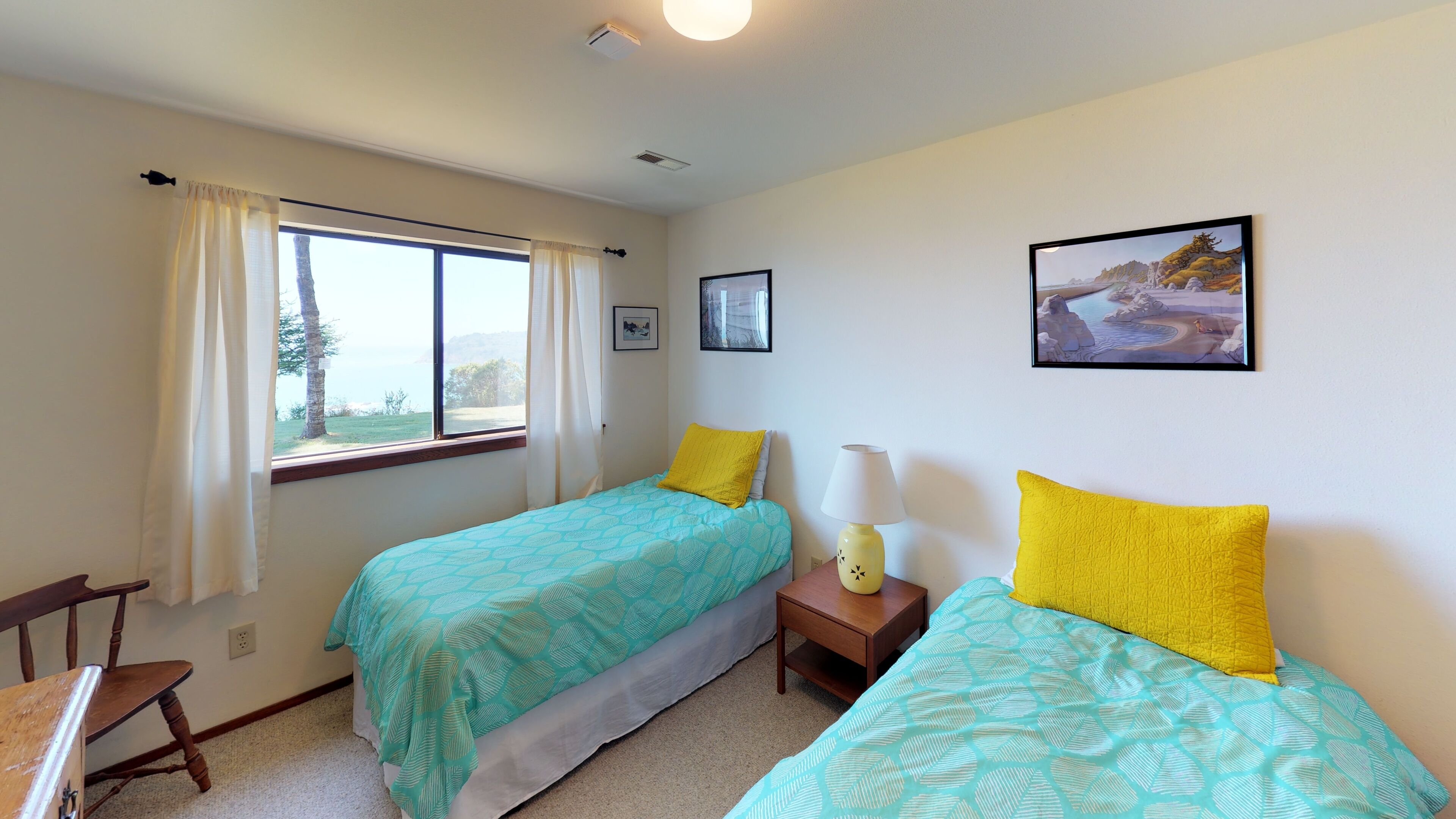 A bedroom with two single beds, a nightstand with a lamp, a chair, and a window with curtains.