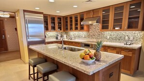 Una cocina moderna con armarios de madera, un refrigerador de acero inoxidable, una encimera de granito y un frutero.