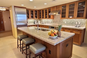 Una cocina moderna con armarios de madera, un refrigerador de acero inoxidable, una encimera de granito y un frutero.