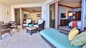 Una habitación de hotel con balcón, muebles de mimbre, televisor y cama.