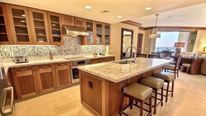 Una cocina amplia con armarios de madera, una isla grande con taburetes de bar y vista al área de estar.