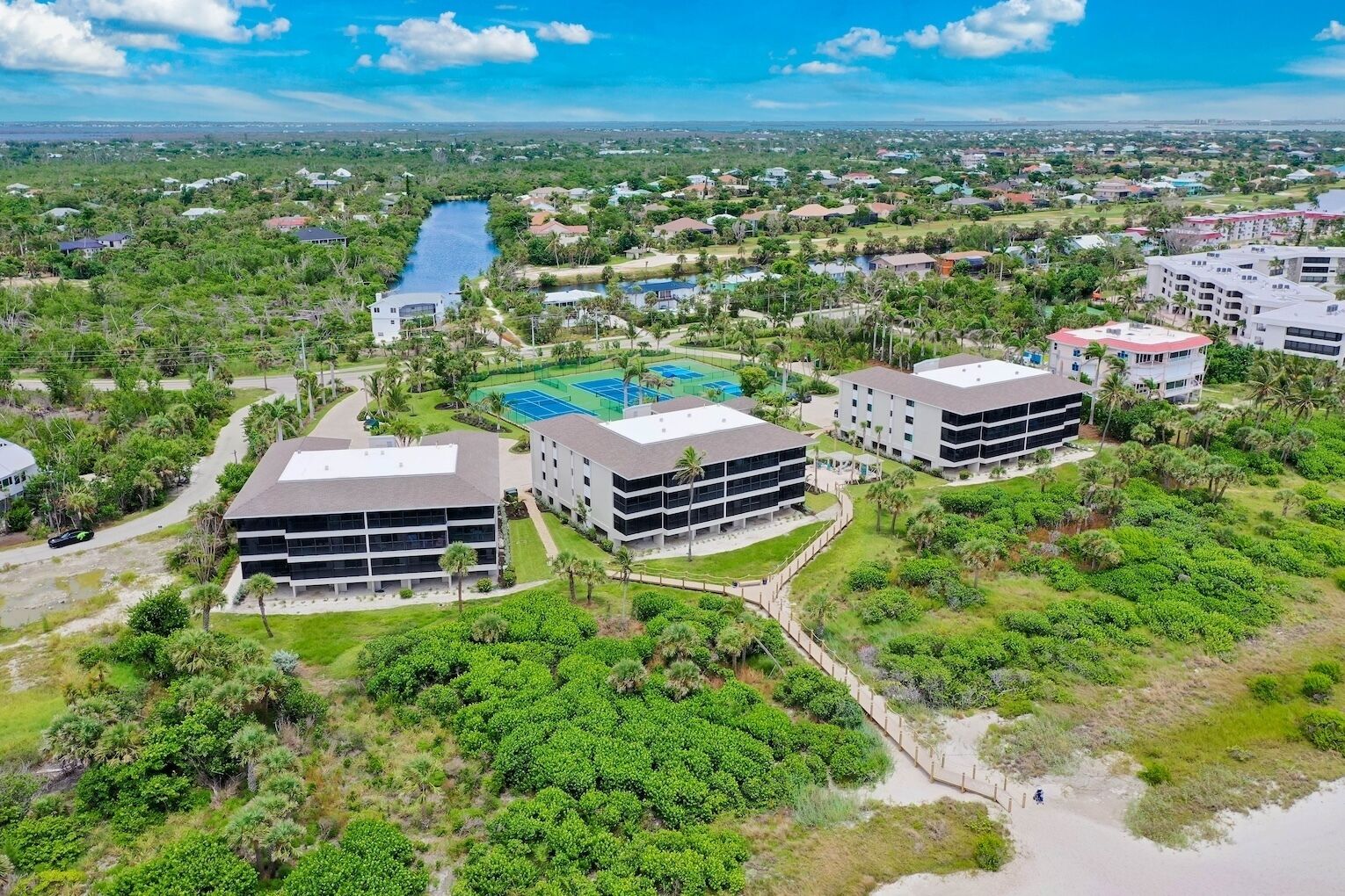 A modern hotel complex with multiple buildings, a central courtyard with a tennis court, and surrounding lush greenery.