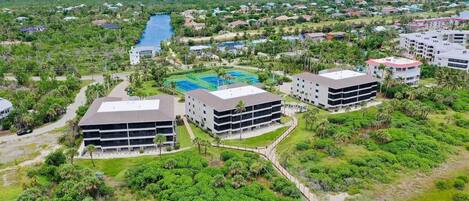 A modern hotel complex with multiple buildings, a central courtyard with a tennis court, and surrounding lush greenery.