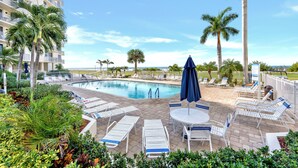 Un área junto a la piscina con sillones de descanso, una piscina y palmeras.