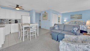 Un espacio habitable compacto con kitchenette, comedor y sala de estar con sofá y reposapiés.