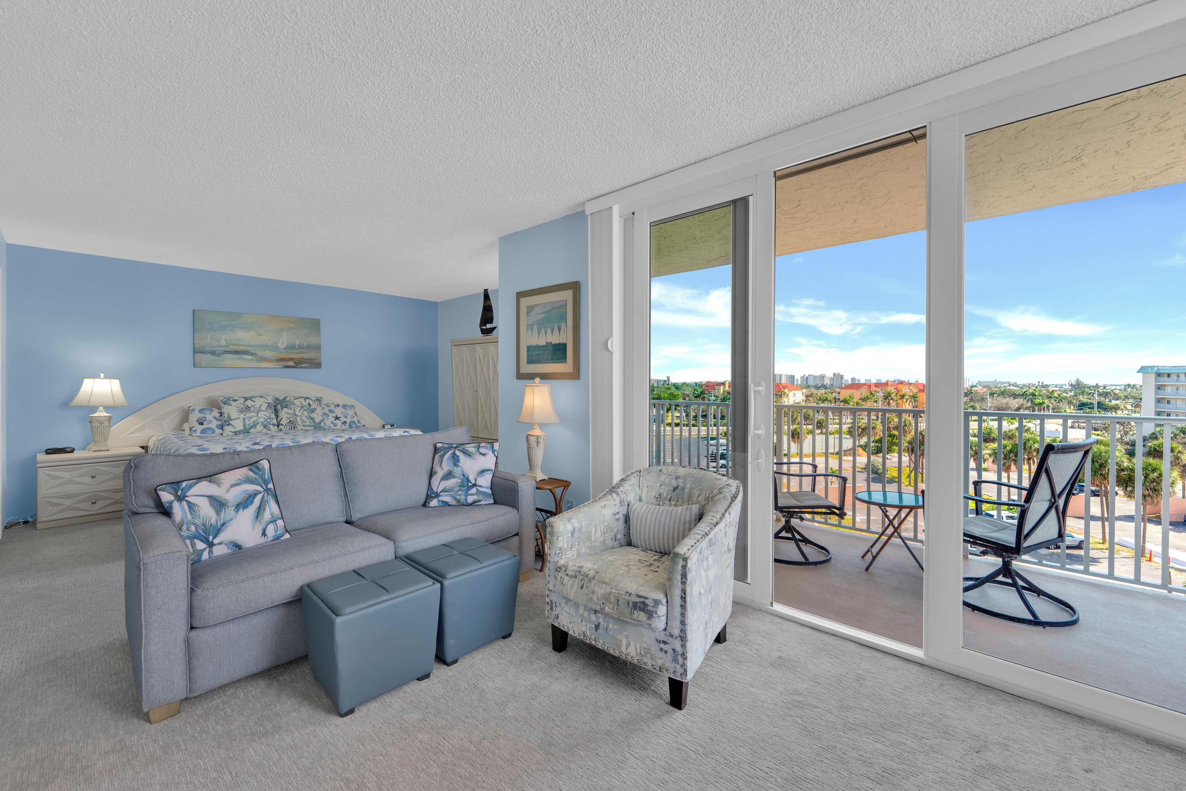 A bedroom with a grey sofa, a matching armchair, and a large window with a city view.