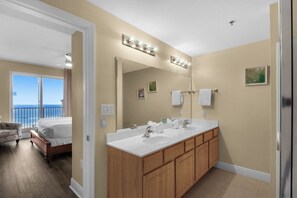 Une salle de bain d’hôtel avec un grand miroir, deux lavabos, des meubles en bois et une vue sur l’océan.