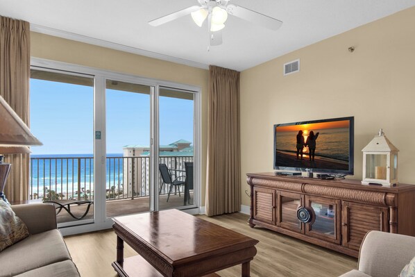Un salon spacieux avec une grande télévision, une table basse en bois et un balcon offrant une vue sur la plage.