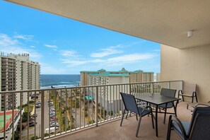 Un balcon avec une table et des chaises, offrant une vue sur la côte, avec des bâtiments et un parking.