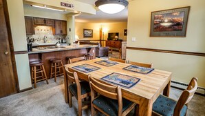 Un coin repas avec une table et des chaises en bois, une cuisine en arrière-plan et un tableau encadré au mur.