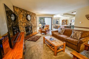 A living room with a stone wall, a fireplace, a sofa, and a coffee table. - Park Place Longs Peak Condo: Easy Access To Main St, Lifts (Breckenridge)