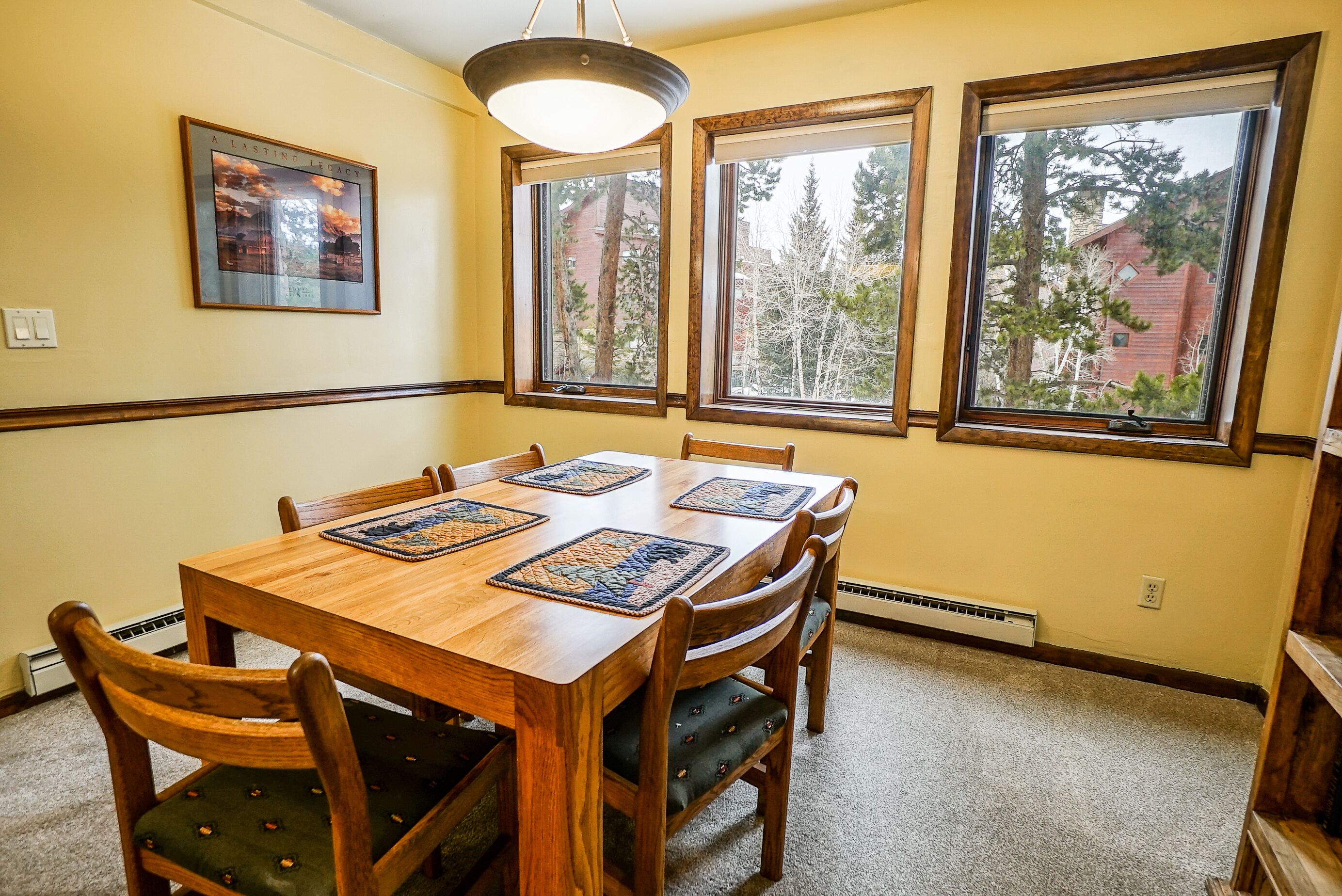 A dining room with a wooden table, chairs, and a large window with a view of trees and a building.