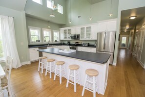Una cocina moderna con una isla grande, taburetes de bar, electrodomésticos de acero inoxidable y armarios blancos.