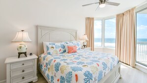 A bedroom with a bed, nightstands, lamps, a ceiling fan, and a large window with curtains. - Open-concept, bright beachfront getaway w/private balcony! (Destin)