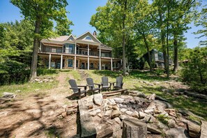 A large house with a stone exterior, multiple balconies, and a fire pit area with Adirondack chairs.