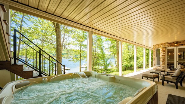 Ein Whirlpool mit Seeblick, eine überdachte Terrasse mit Gartenmöbeln und eine Treppe, die zu einer oberen Ebene führt.