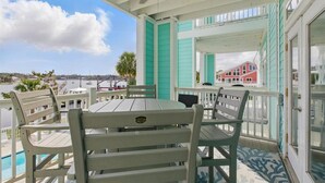 A covered outdoor seating area with a table and chairs, overlooking a body of water and buildings. - Remodeled! Waterfront, Rivers Edge Condo #1C-Bldg 1 *DOCK w/ASSIGNED BOAT SLIP! (Steinhatchee)