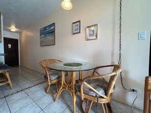 A dining area with wicker chairs and a glass table, a door, and wall-mounted artwork.