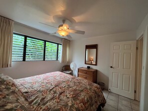 A bedroom with a bed, a dresser, a mirror, a ceiling fan, and a window with blinds.