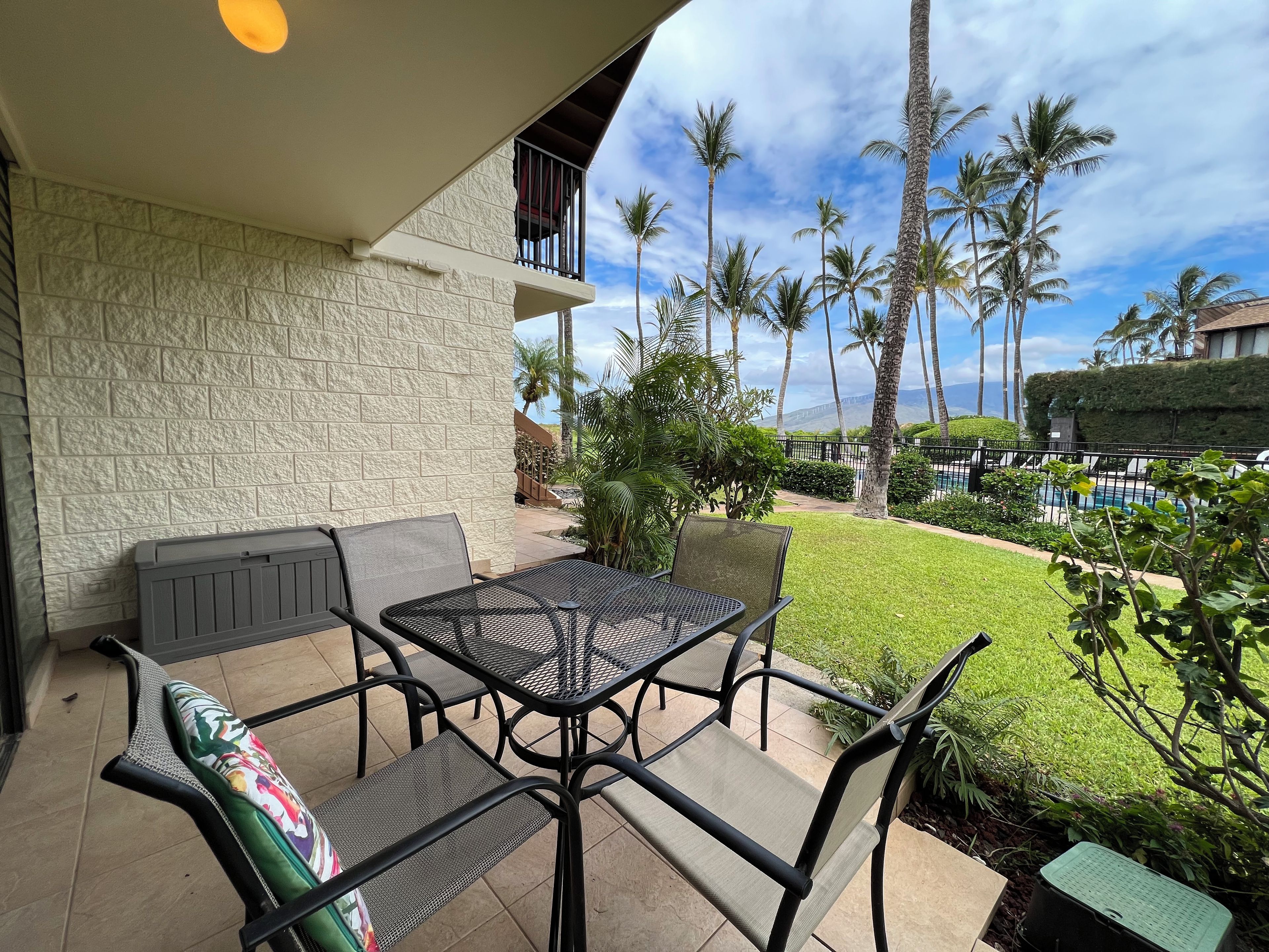 Une terrasse avec une table et des chaises, un mur en pierre et une vue sur des palmiers et une piscine.