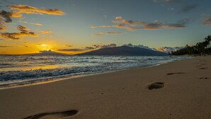 Una playa con huellas que conducen al agua, un atardecer y una montaña al fondo.
