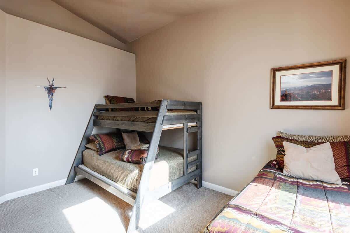 A bunk bed with a ladder, a single bed with a patterned bedspread, a framed picture on the wall, and a wall-mounted decoration.