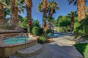 A pool area with palm trees, lounge chairs, and a hot tub.