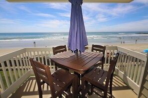 An outdoor seating area with a table and chairs, overlooking a beach with people and waves. - Absolute Beach Front Cottage! Panoramic Views E20 North Coast Village (Oceanside)
